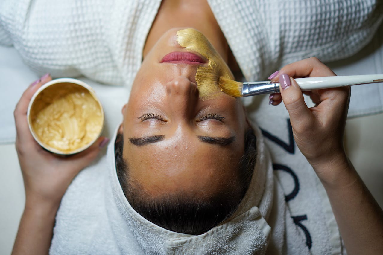 services-02 A woman enjoying a gold facial mask for relaxation and skincare at a spa.